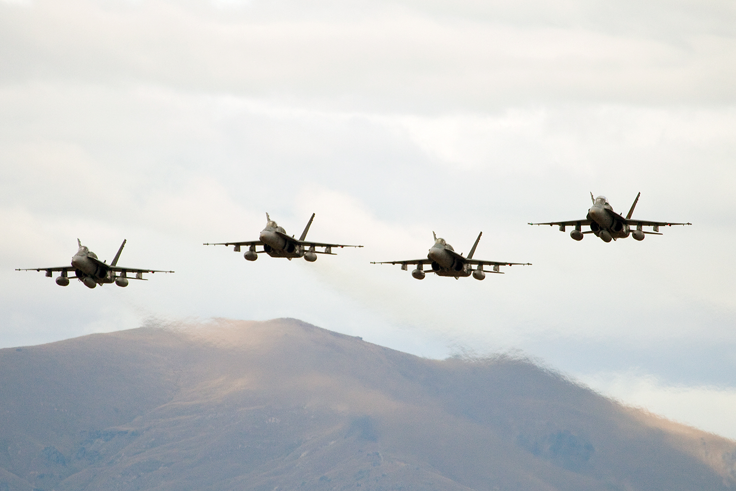 Four F-18 aircrafts flying over an mountainous region